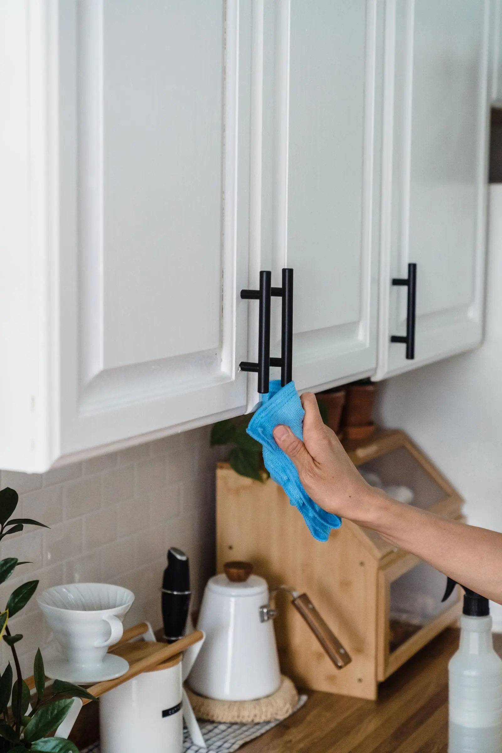 A hand wiping down a kitchen cabinet door and handle with a cloth.